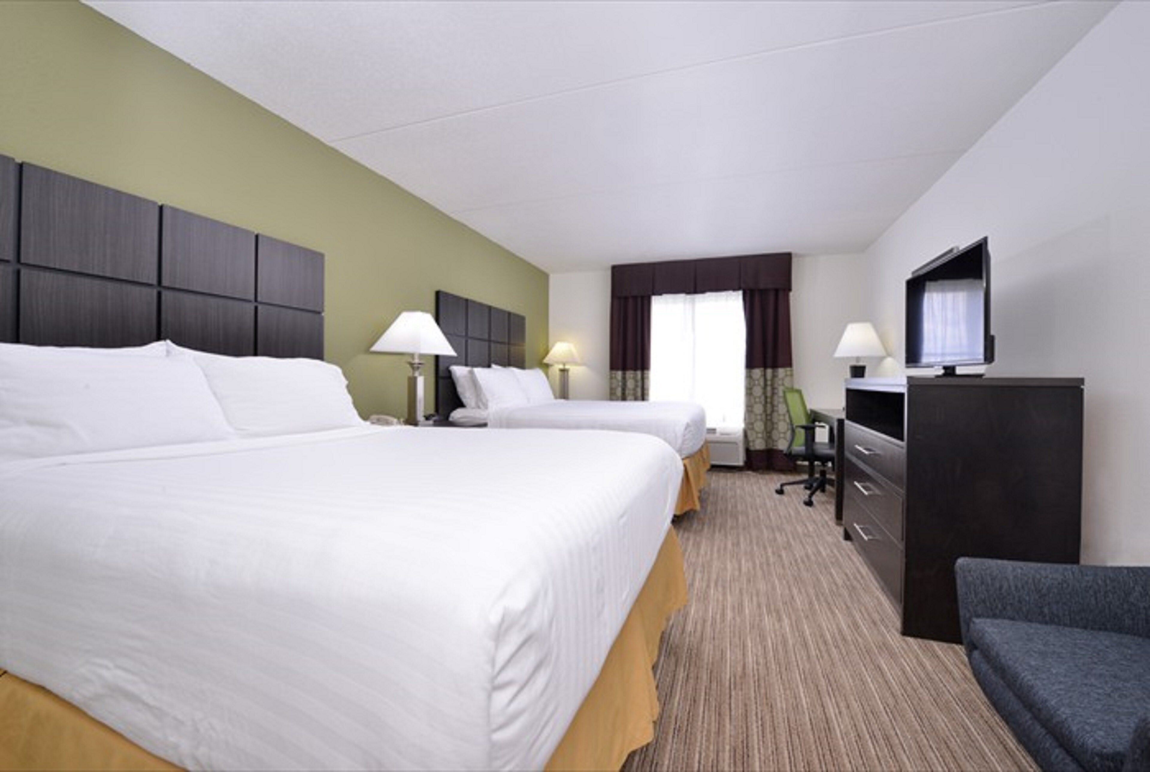 A hotel room with two beds, a desk, a television, and a chair.