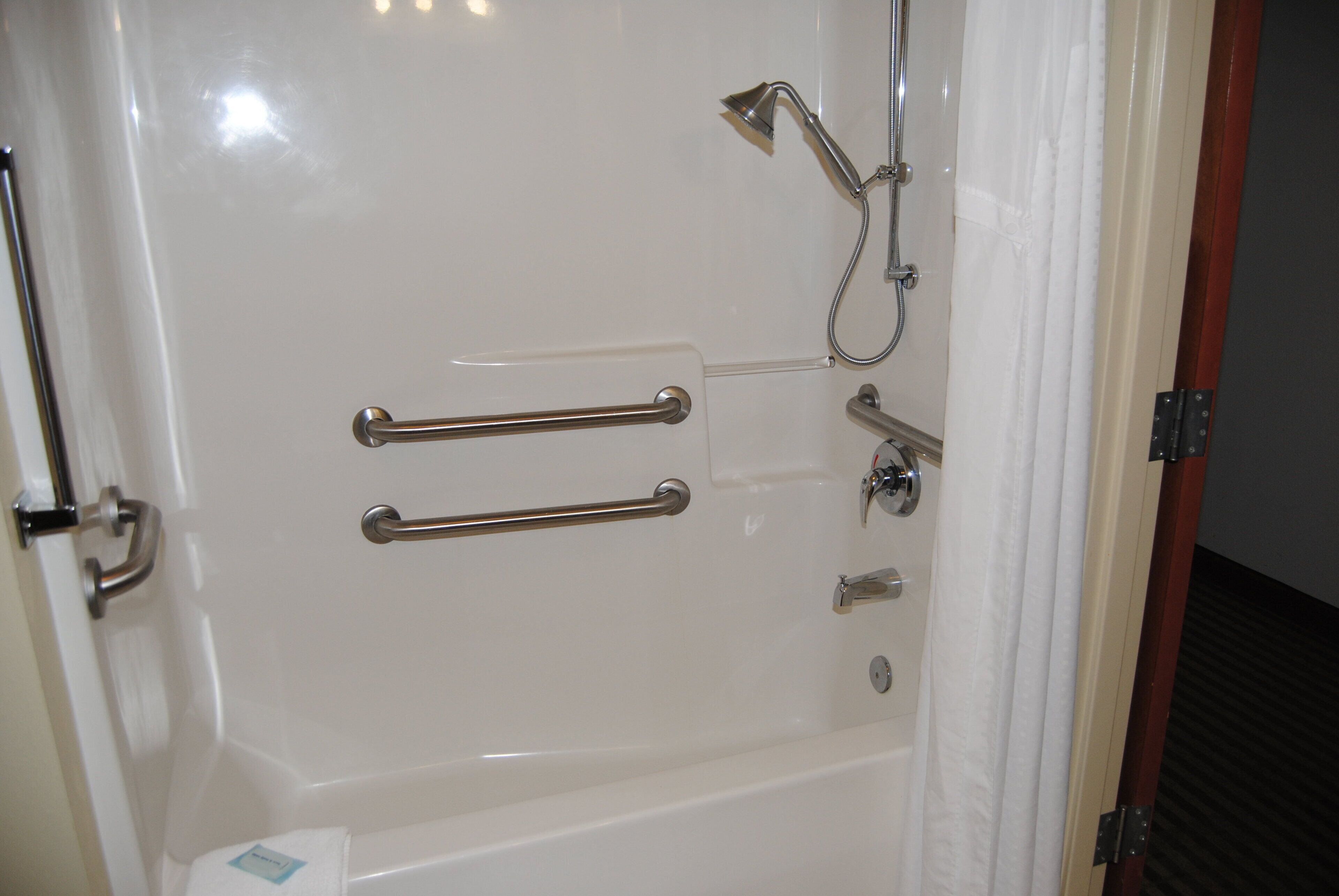 A bathroom with a bathtub, grab bars, a shower head, and a towel rack.