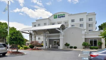 Un hotel Holiday Inn Express con entrada cubierta, estacionamiento y cielo despejado.