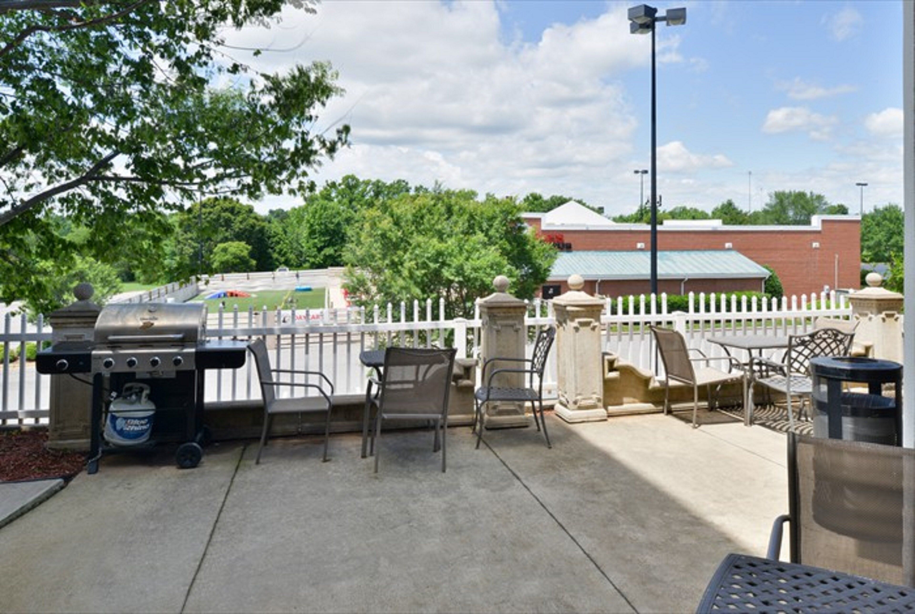 An outdoor patio with a grill, chairs, and a trash can.
