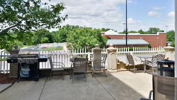 An outdoor patio with a grill, chairs, and a trash can.