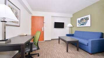 A hotel room with a desk, chair, sofa, TV, and artwork on the walls.