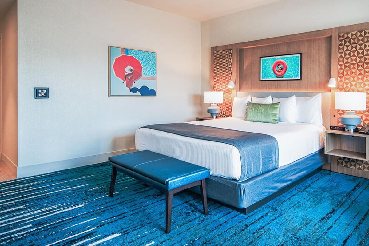 A hotel room with a large bed, a bench, two bedside tables with lamps, and a chair.