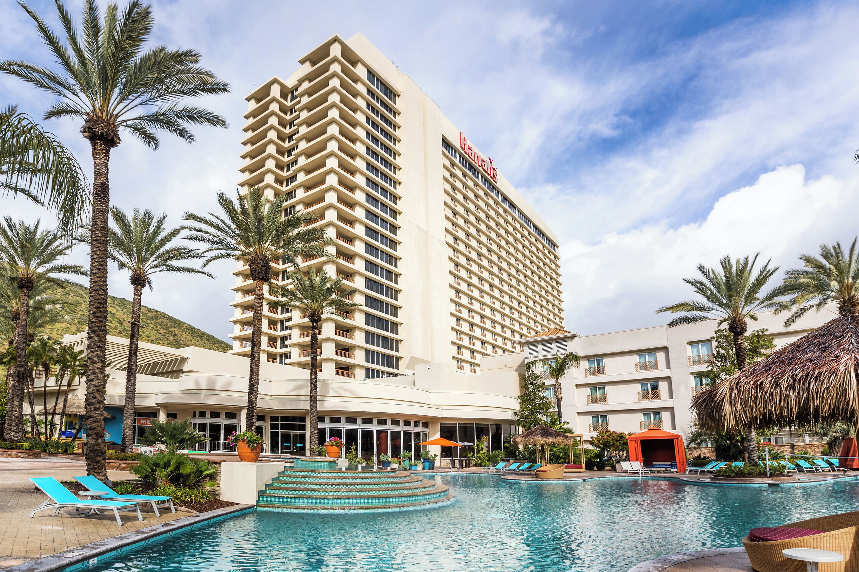 A hotel with a swimming pool, palm trees, and a mountain in the background.