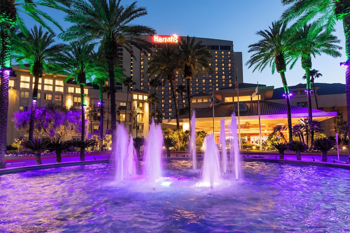 A hotel with a fountain, palm trees, and a neon sign.