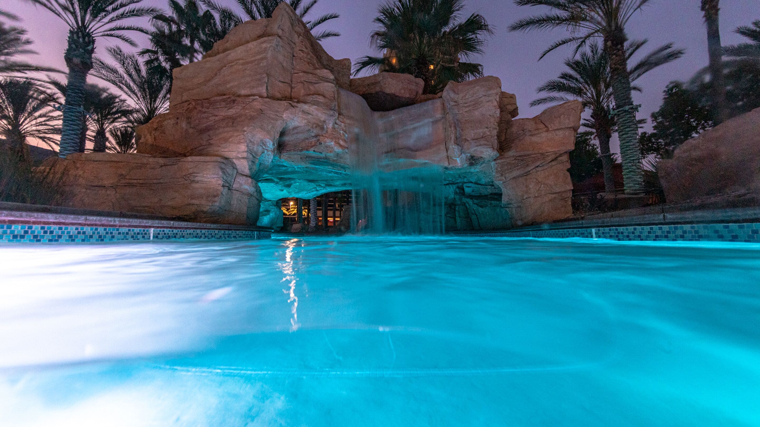 A pool with a waterfall feature, surrounded by large rock formations and palm trees.