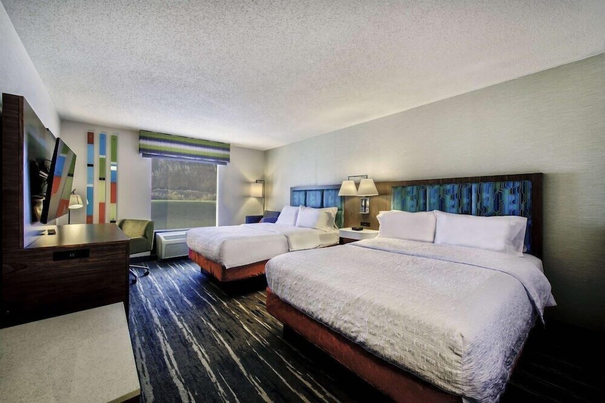 A hotel room with two beds, a desk, a chair, a TV, and a window with a view.