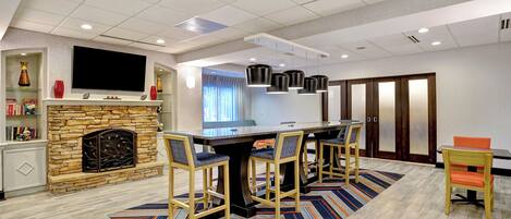 A modern kitchen with a stone fireplace, a dining table with chairs, and a flat-screen TV mounted above the fireplace.