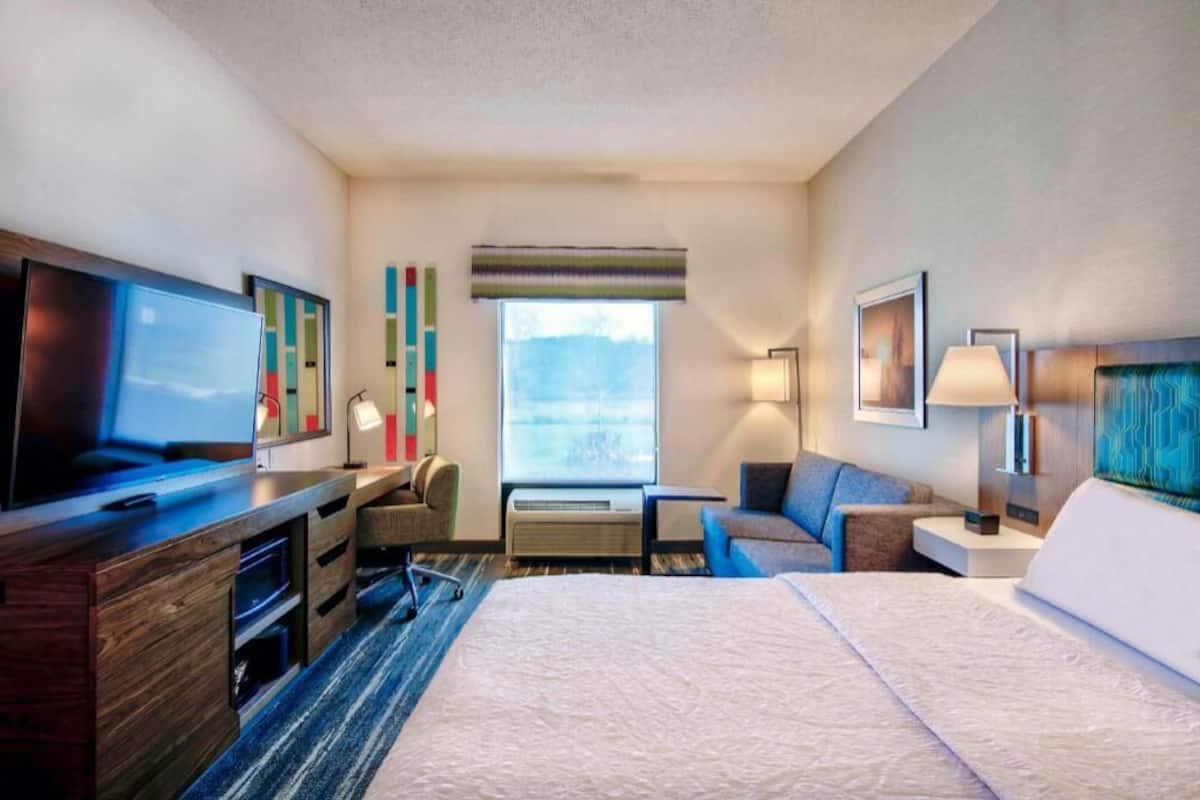 A hotel room with a bed, a desk, a TV, a window, and a view of the outdoors.
