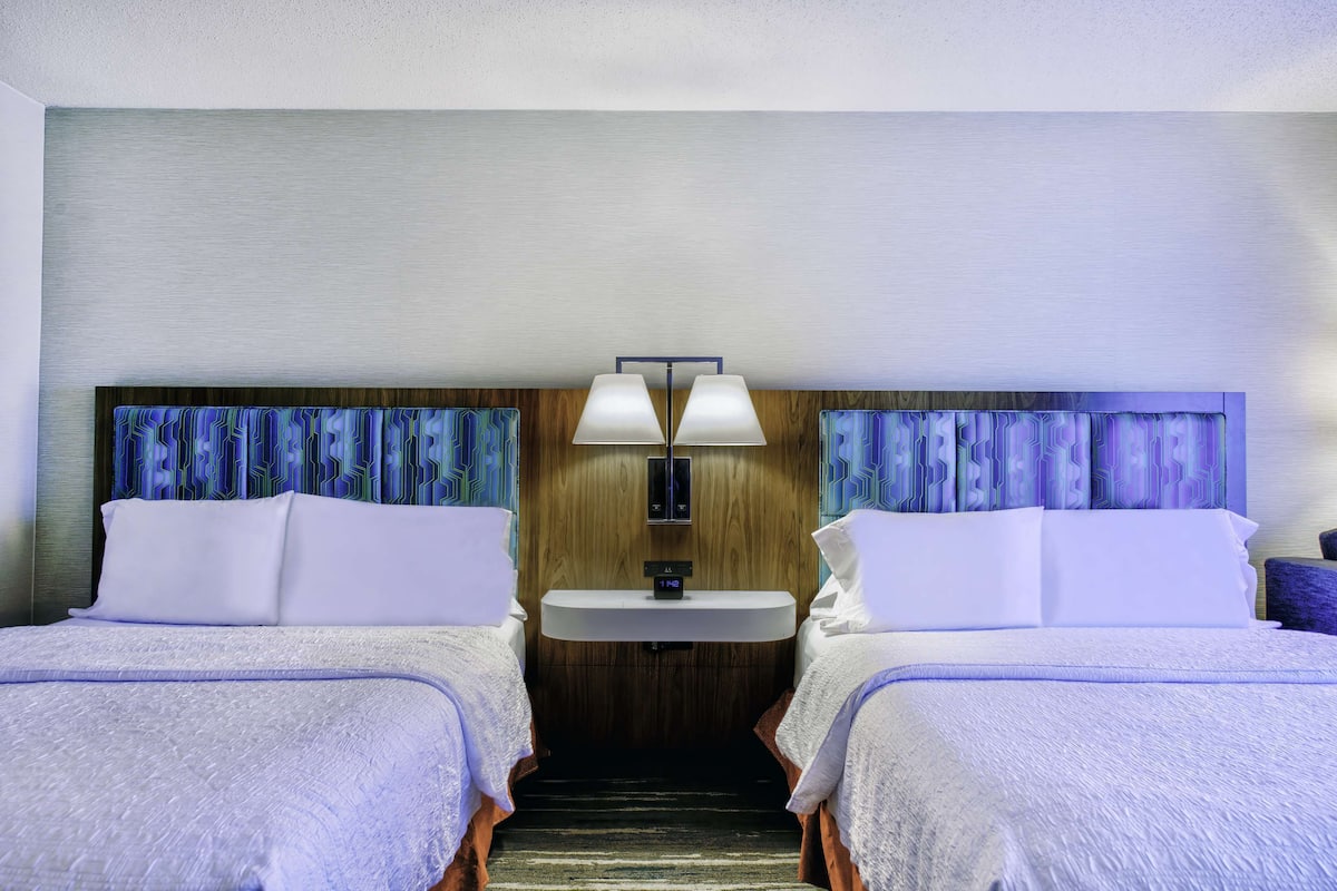 A hotel room with two beds, a small sink, and a mirror.