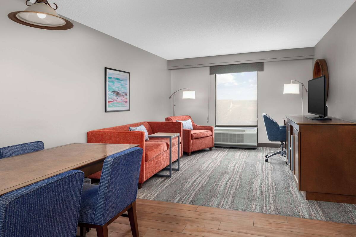 A hotel room with a dining area, two sofas, a desk, and a television.