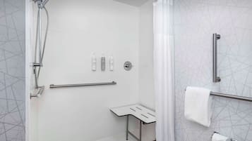 A modern bathroom with a shower, toilet paper, and handrails.