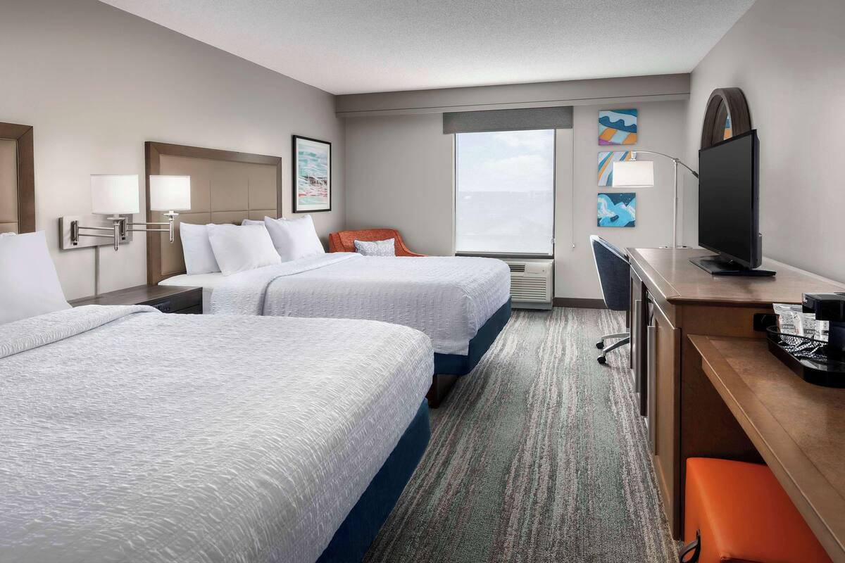 A hotel room with two beds, a desk, a television, and artwork on the walls.