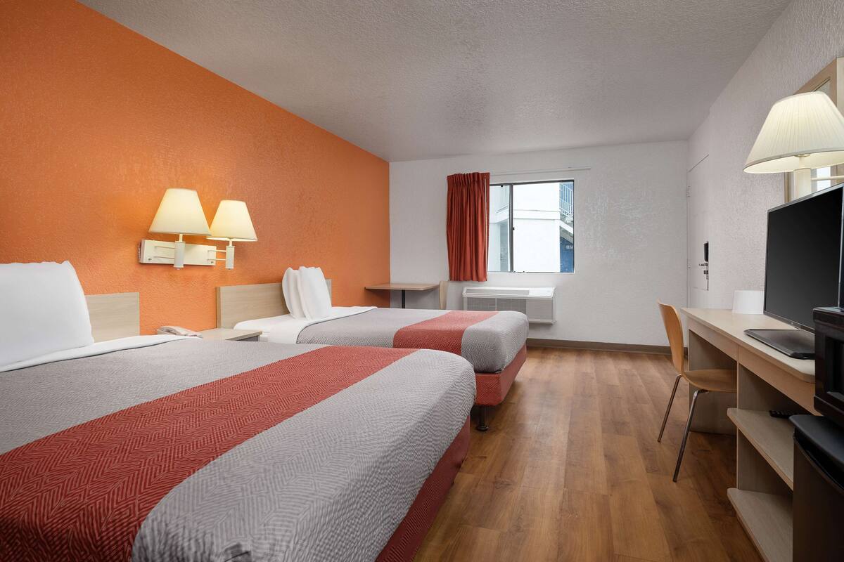 Une chambre d’hôtel avec deux lits, un bureau, une chaise, une télévision et une fenêtre avec des rideaux.