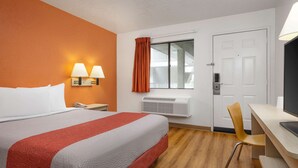 Une chambre d’hôtel avec un lit, un bureau, une chaise, une fenêtre avec des rideaux et un radiateur.