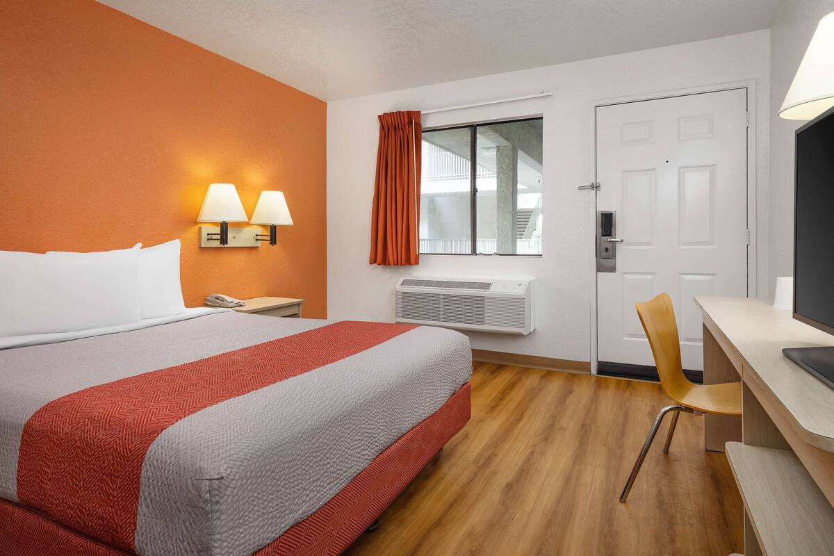 Une chambre d’hôtel avec un lit, un bureau, une chaise, une fenêtre avec des rideaux et un radiateur.