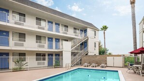 Un hôtel à plusieurs étages doté d’un espace piscine comprenant une piscine, des chaises longues et un escalier menant aux étages supérieurs.
