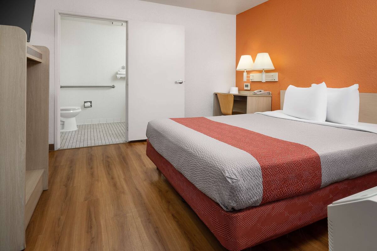 Une chambre d’hôtel comprenant un lit, un bureau avec une lampe, une salle de bain avec des toilettes et un espace douche.