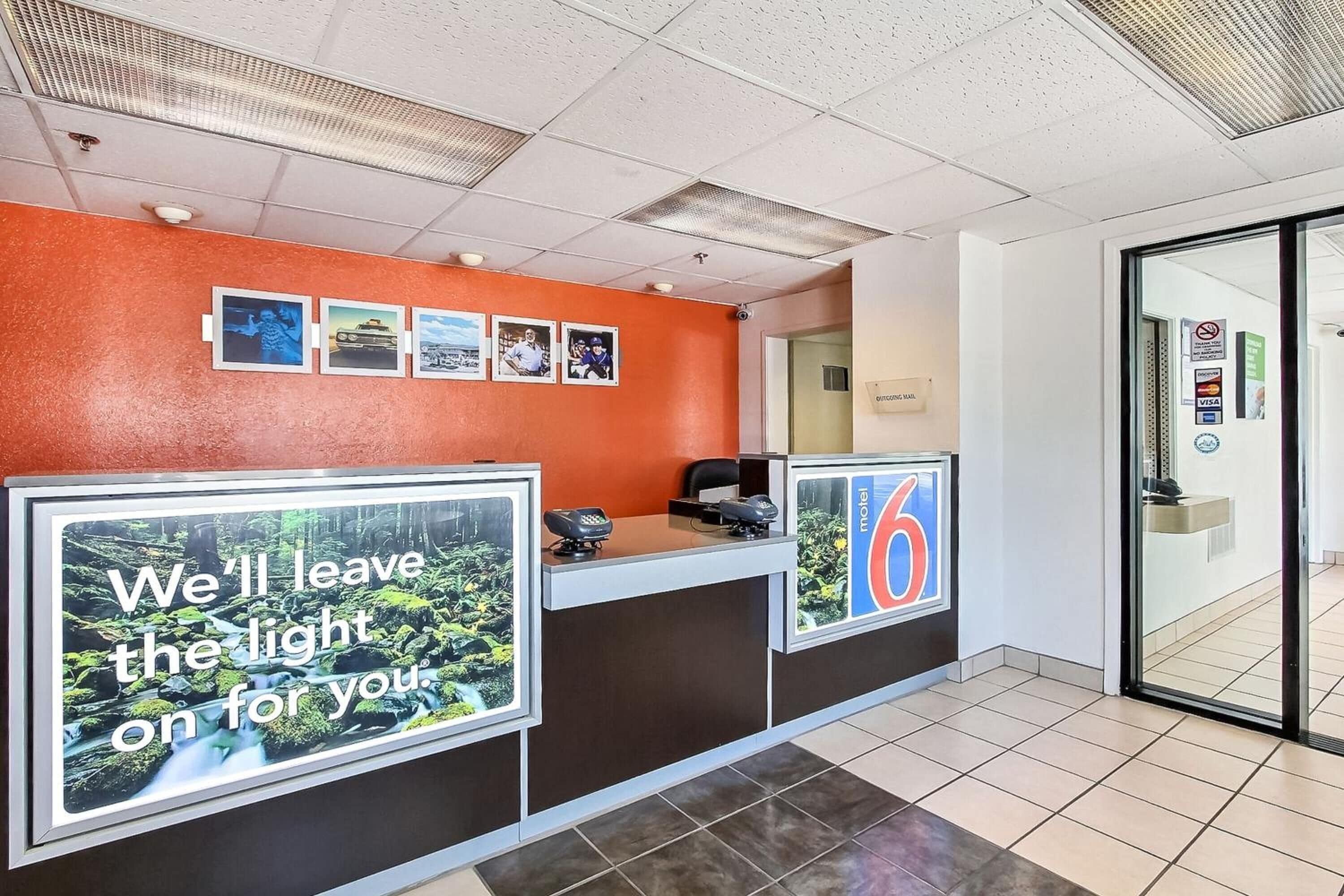 Un espace d’accueil d’hôtel au design moderne, comprenant un comptoir d’accueil, un écran numérique affichant une image panoramique et un panneau indiquant le numéro de la chambre 6.