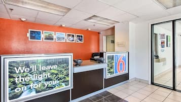 Un espace d’accueil d’hôtel au design moderne, comprenant un comptoir d’accueil, un écran numérique affichant une image panoramique et un panneau indiquant le numéro de la chambre 6.