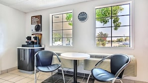 Un petit café moderne avec deux fauteuils en cuir noir, une table ronde, un appareil à café, une horloge et de grandes fenêtres donnant sur l’extérieur.