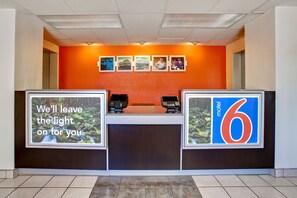A hotel reception desk with a modern design, featuring a large number '6' sign, a digital display, and a series of framed pictures on the wall. - Motel 6 Sunnyvale, CA - North (Sunnyvale)