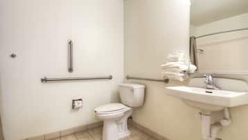 Un baño con inodoro, barras de apoyo, lavamanos y toallero.