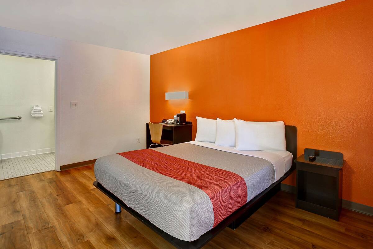 A modern hotel room with a large bed, a nightstand, a bedside table, and a wall-mounted light.