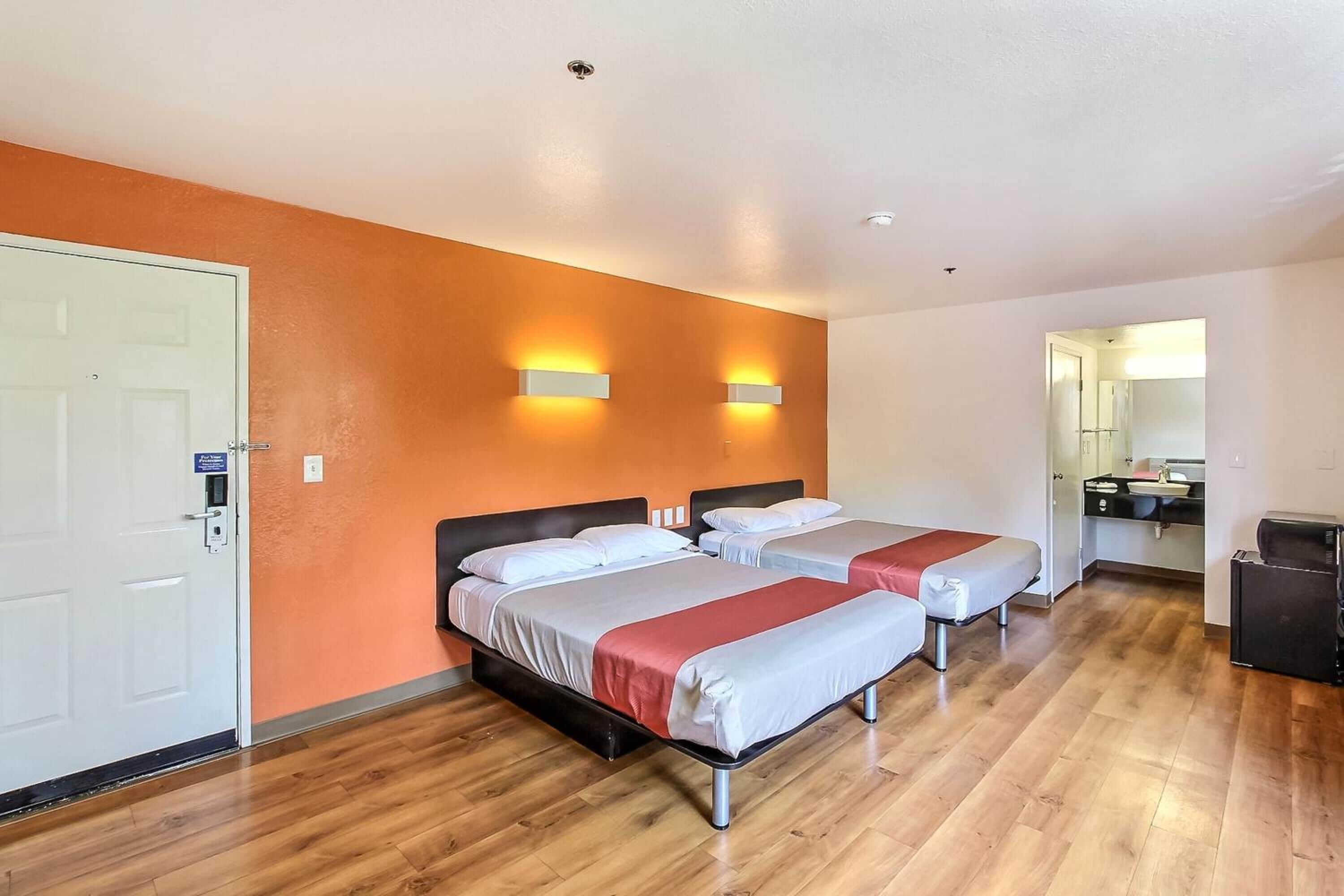 A hotel room with two beds, a kitchenette, and a bathroom visible through an open door.