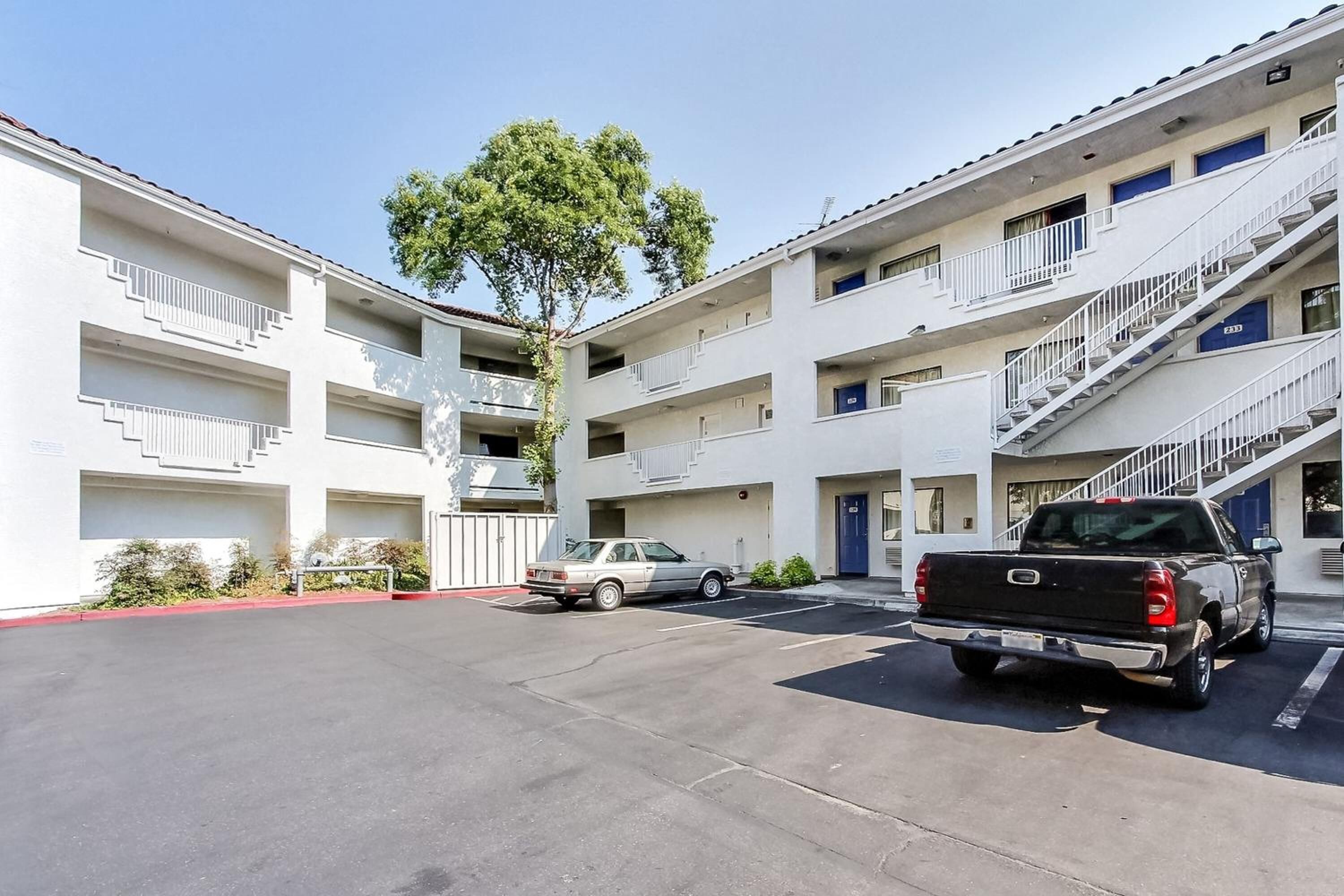 A multi-story motel with a parking lot, a tree, and two parked vehicles.