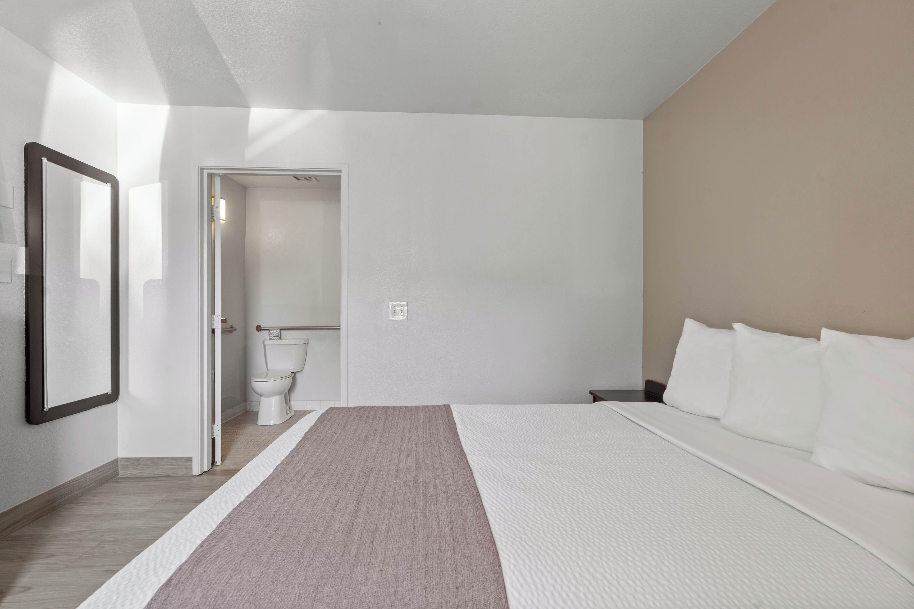 A modern bedroom with a large bed, a bedside table, a mirror, and a view of the bathroom.