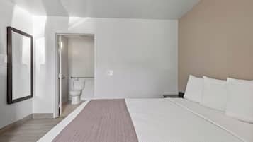 A modern bedroom with a large bed, a bedside table, a mirror, and a view of the bathroom.