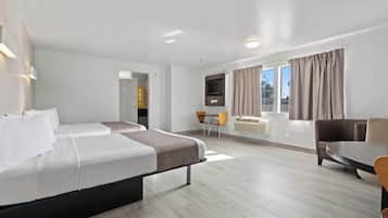 A hotel room with two beds, a dining area, a TV, and a window with curtains.