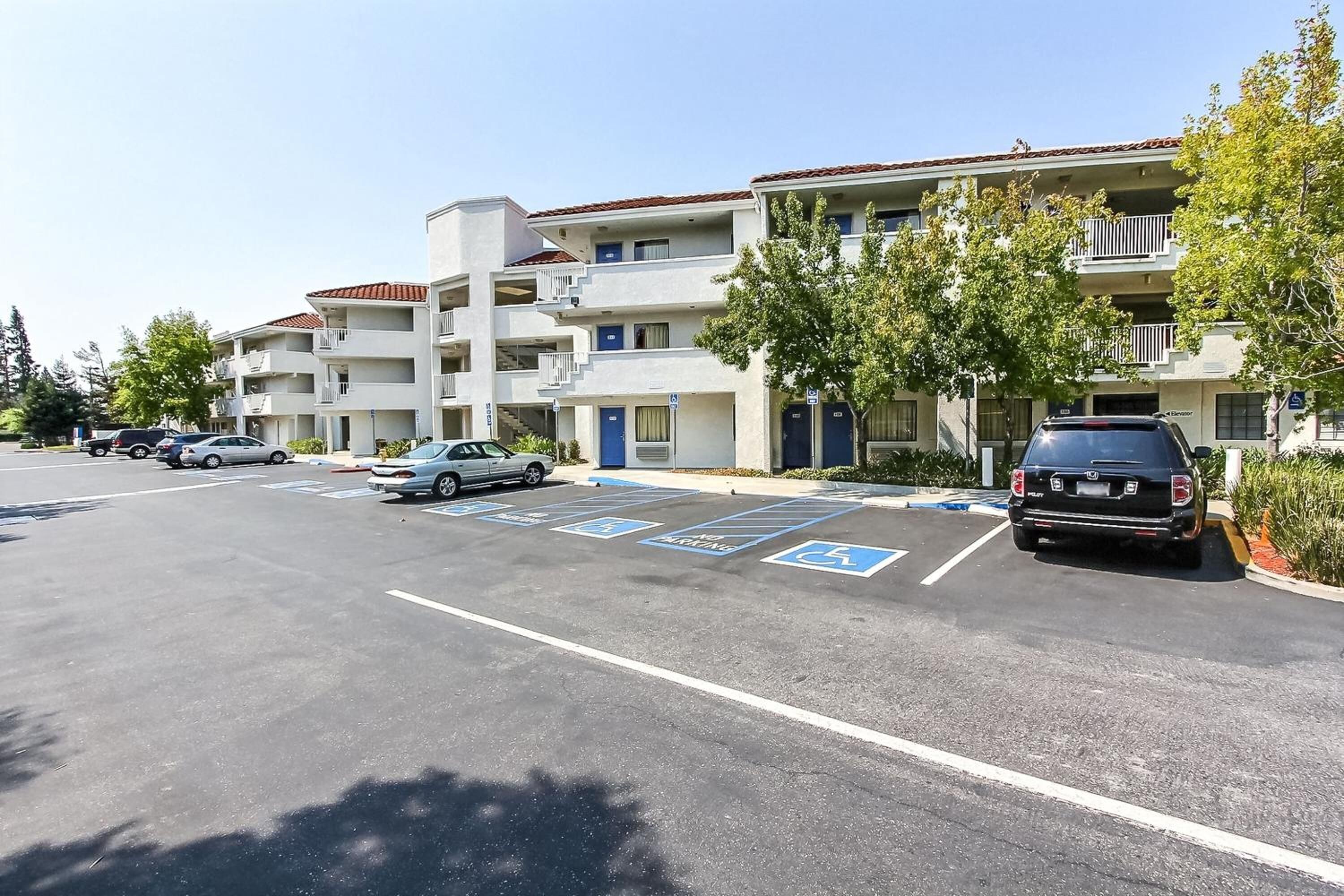 A parking lot with marked handicapped spaces and a row of multi-story buildings with balconies.