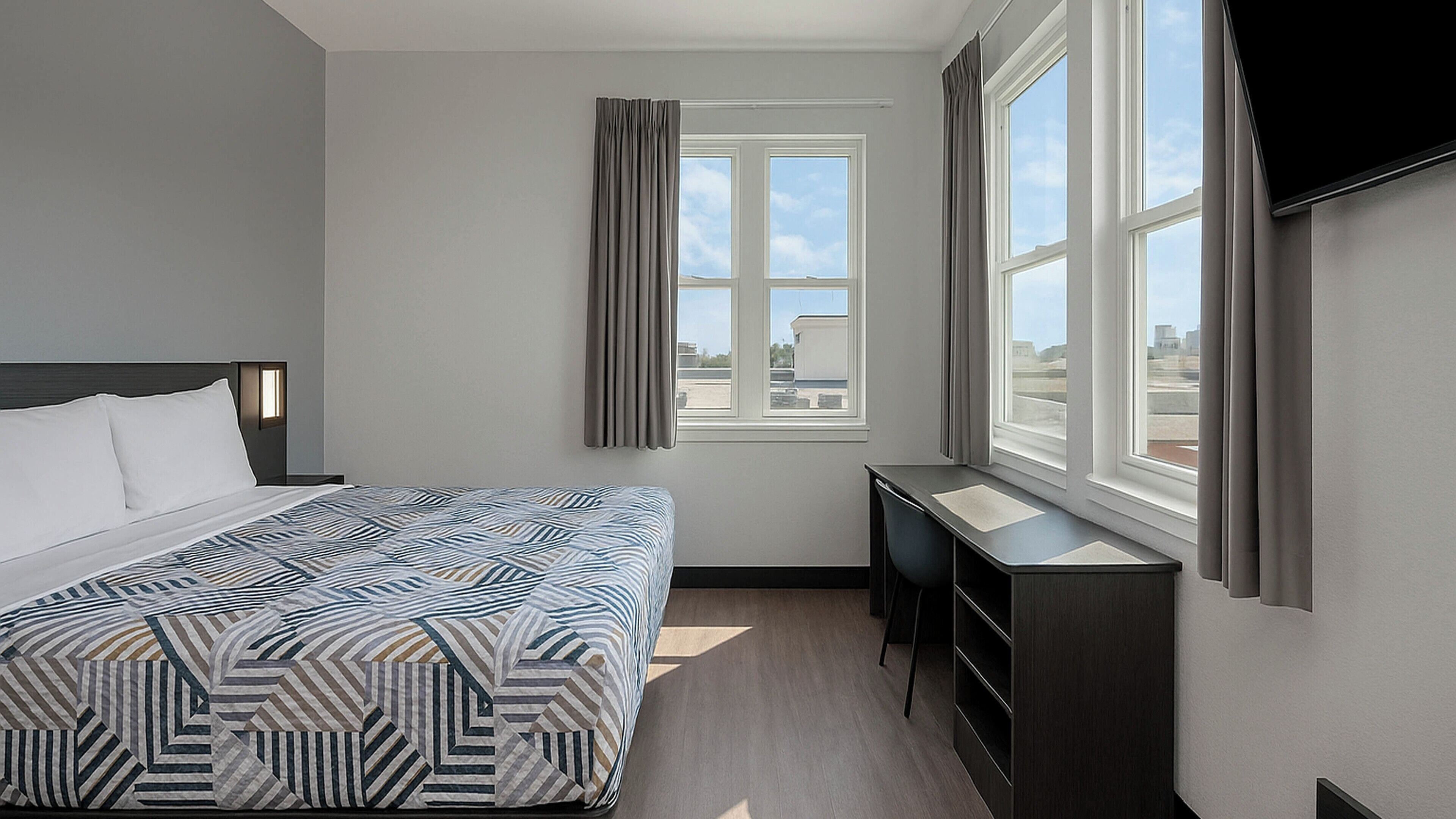 Una camera d'albergo con un letto, una scrivania e una finestra con tende.