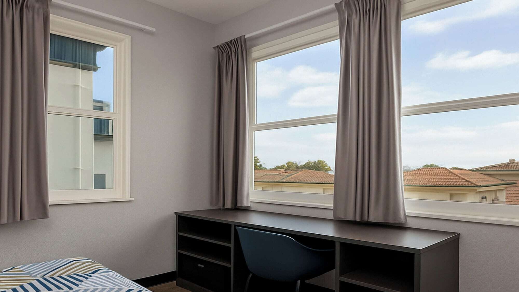 A bedroom with a bed, a desk with a chair, and a window with curtains.