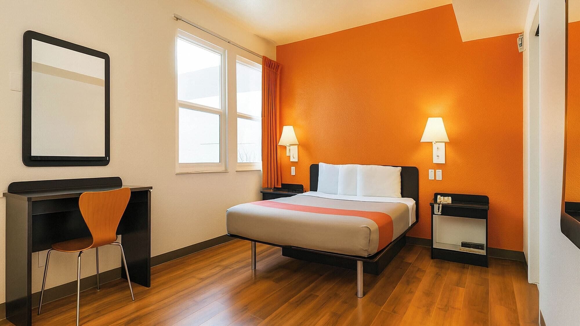 Habitación de hotel con cama, escritorio, silla, dos lámparas de noche y ventana.
