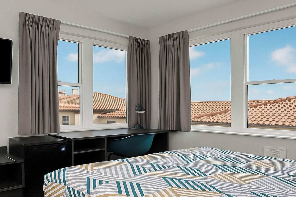 A hotel room with a bed, a desk, a chair, and a TV.