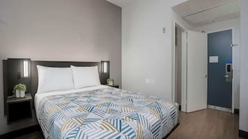 Habitación de hotel con una cama, mesitas de noche, una lámpara de pared y una puerta.