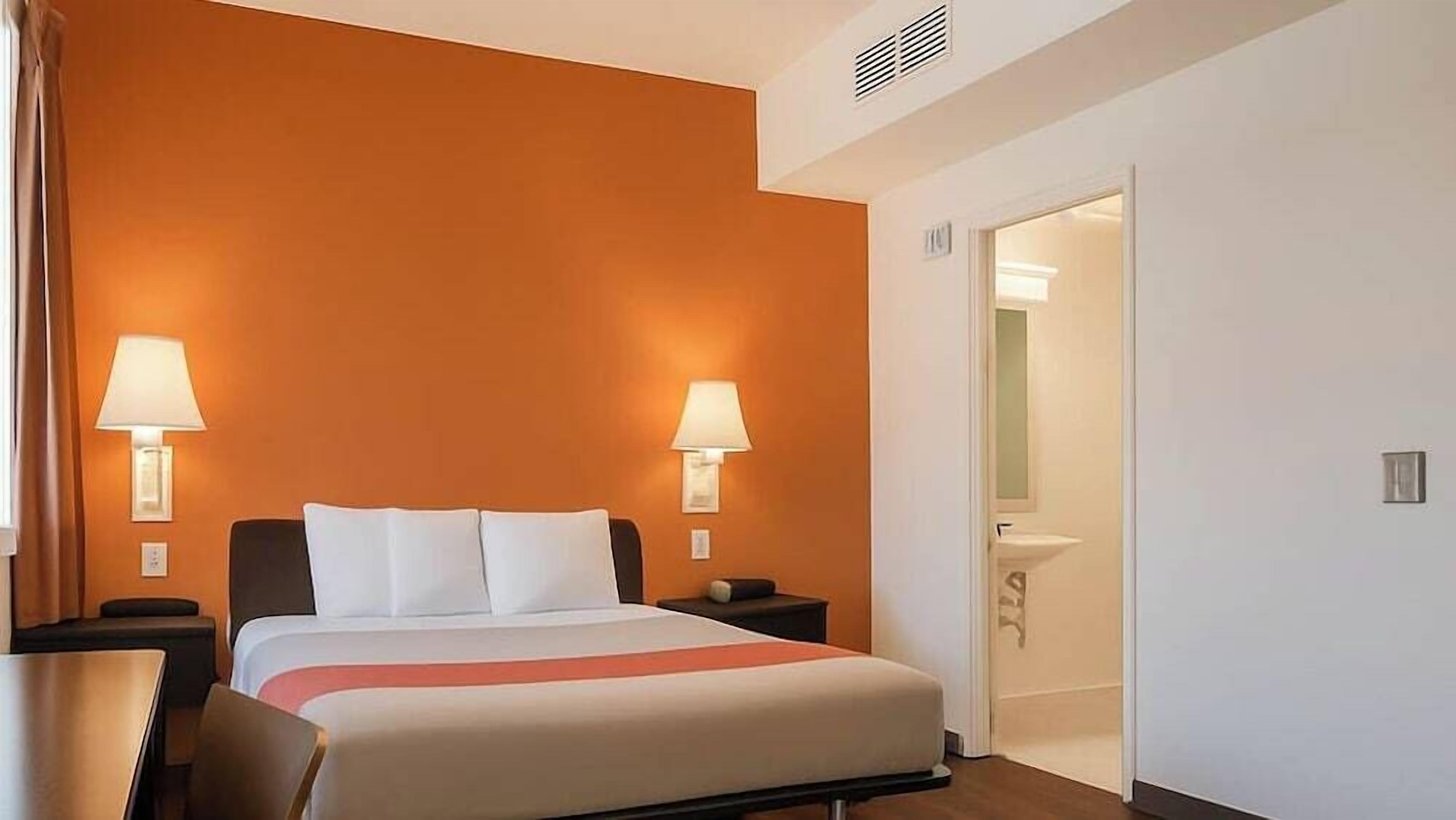 Une chambre d’hôtel avec un lit, deux lampes de chevet, une table de chevet, un bureau et une salle de bain visible à travers une porte ouverte.