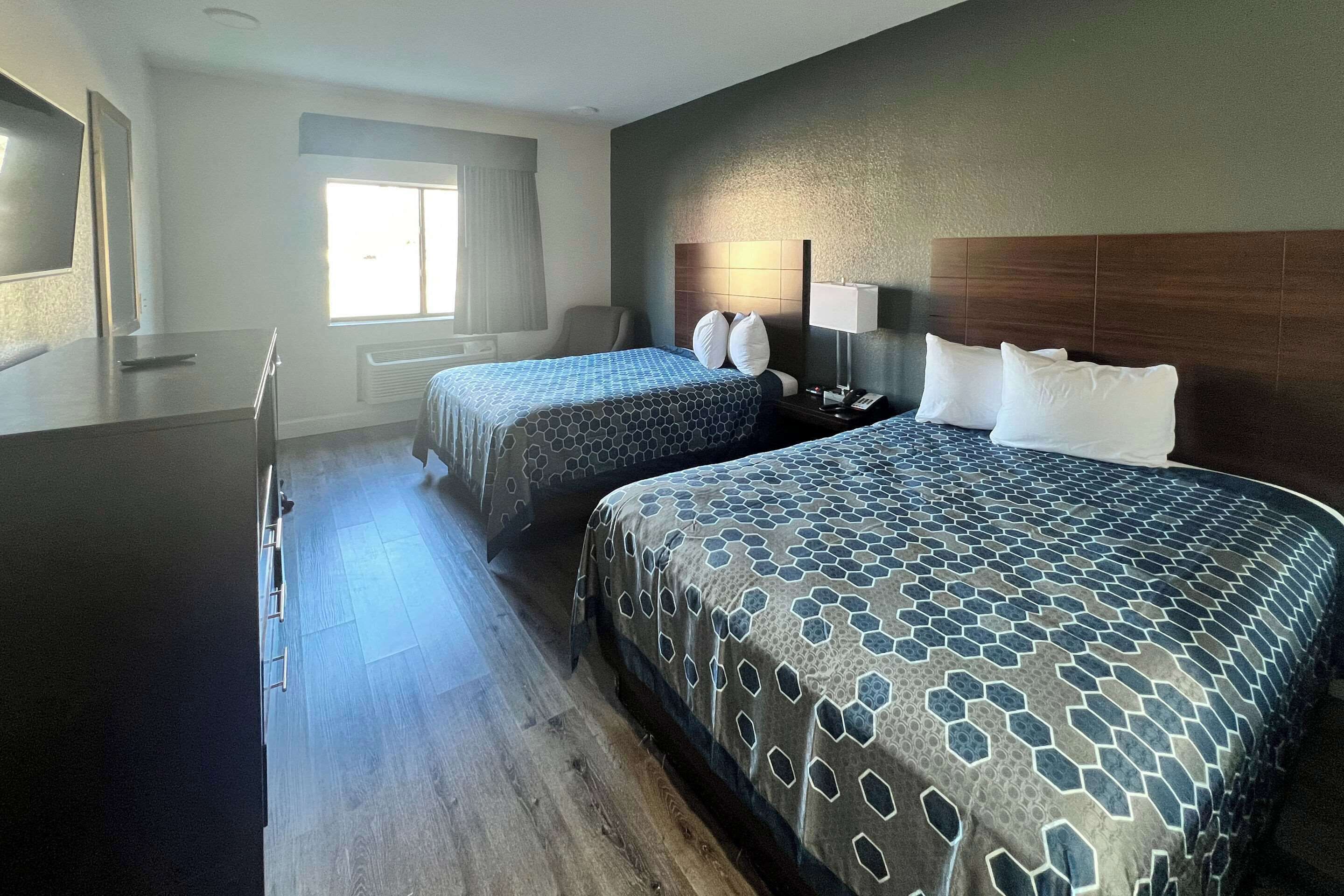 Quarto de hotel com duas camas, uma mesa, uma cadeira e uma janela.