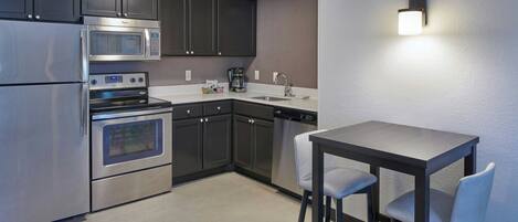 A modern kitchen with stainless steel appliances, dark cabinets, and a small dining area with two chairs.
