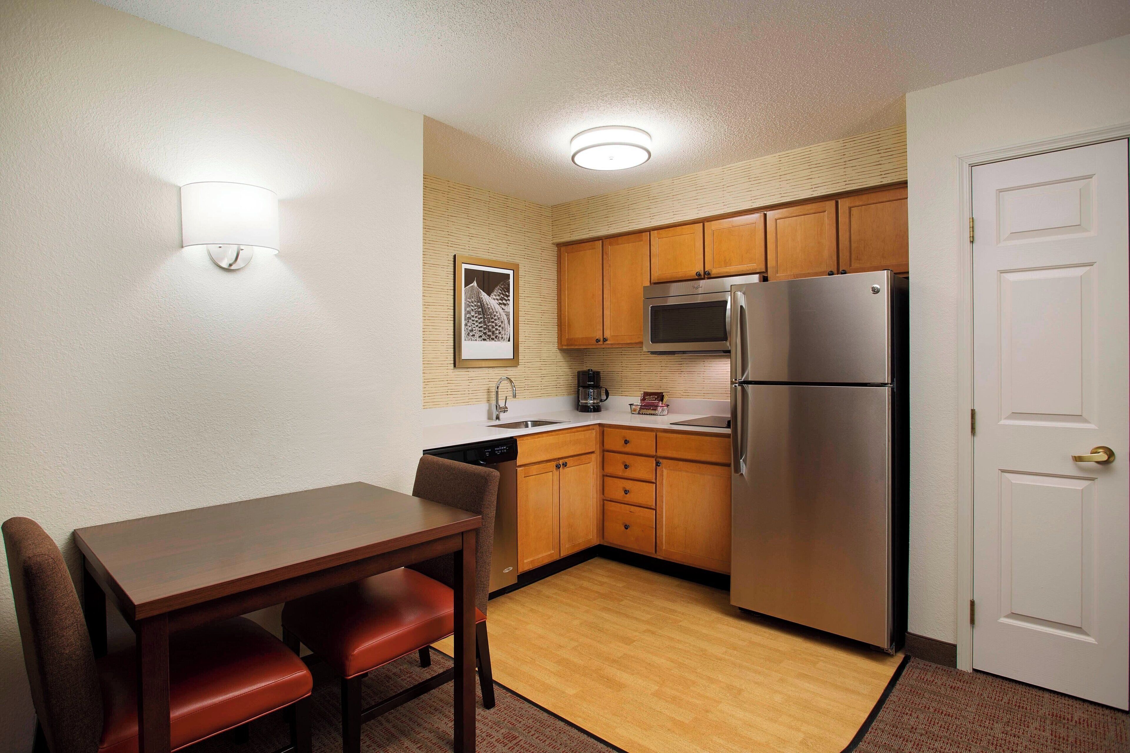 A compact kitchen with wooden cabinets, a stainless steel refrigerator, and a dining table with chairs.