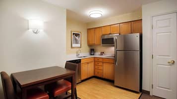 A compact kitchen with wooden cabinets, a stainless steel refrigerator, and a dining table with chairs.