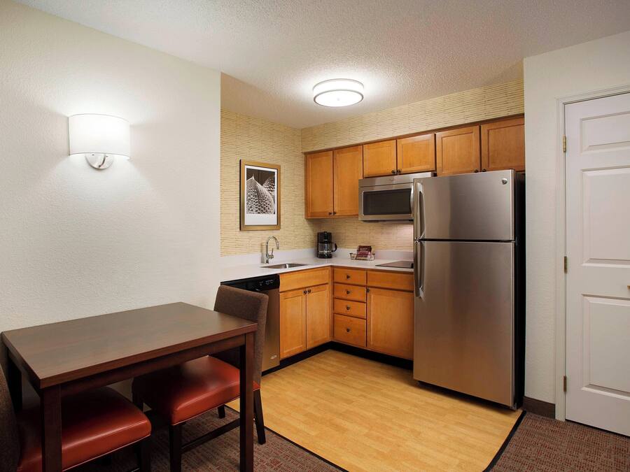 A compact kitchen with wooden cabinets, a stainless steel refrigerator, and a dining table with chairs.