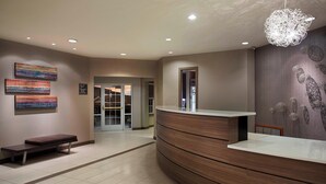 A reception area with a curved wooden counter, a bench, and a wall with abstract art. - Residence Inn by Marriott Detroit Novi (Novi)