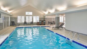 An indoor swimming pool with clear blue water, surrounded by lounge chairs and a small seating area with tables. - Residence Inn by Marriott Detroit Novi (Novi)
