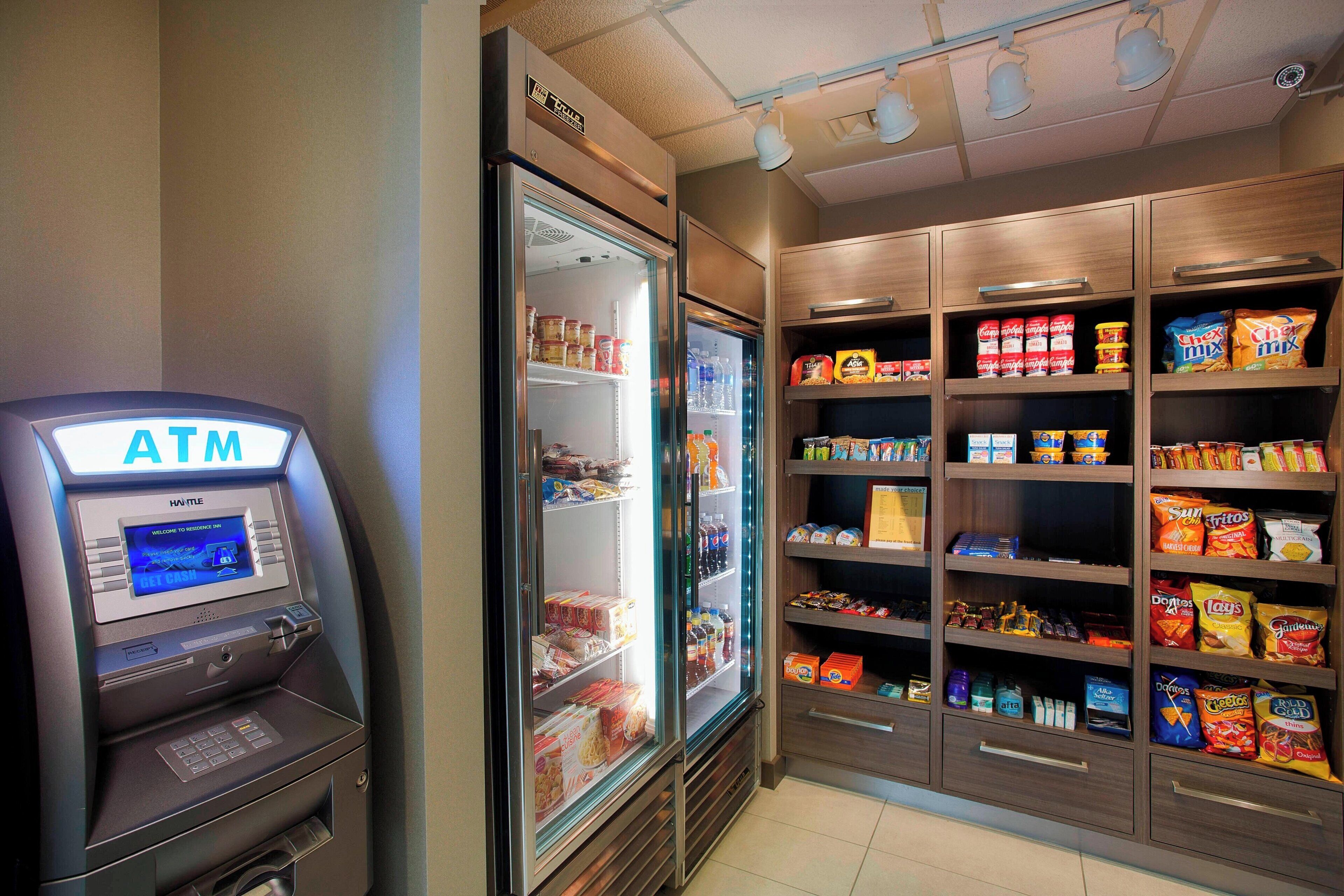 Un distributeur automatique de billets, des vitrines réfrigérées et des étagères remplies de collations et de boissons.