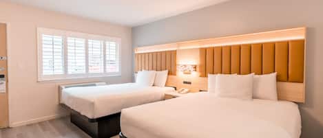 A hotel room with two beds, a large window, and a modern headboard.