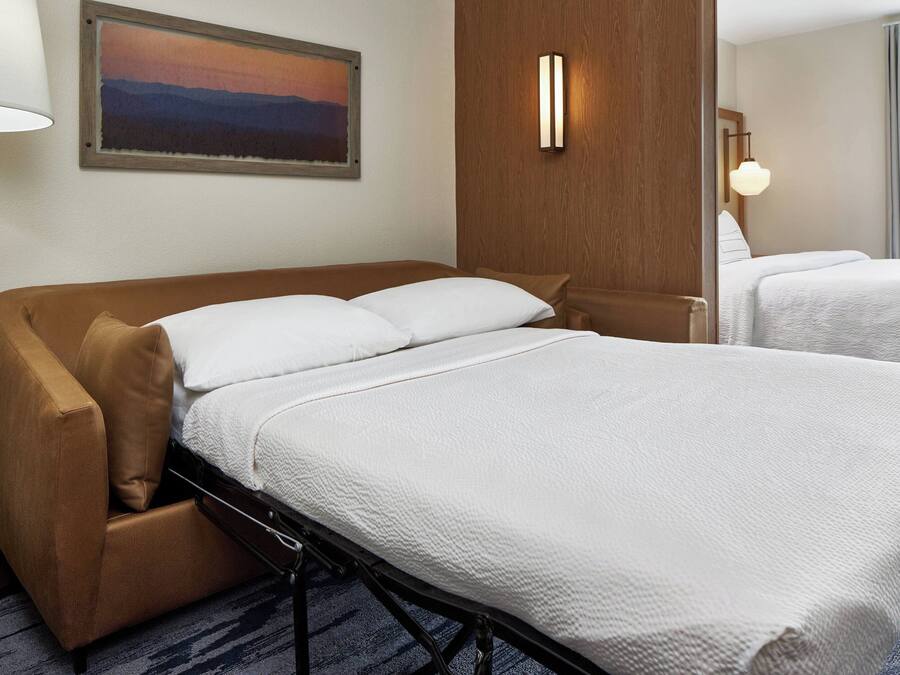 A hotel room with a bed, a chair, a painting, and a lamp.